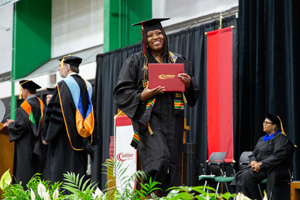 New Gateway graduate in cap and gown shows off her diploma as she walks across the stage.
