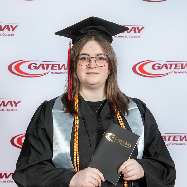 Karley Webb at commencement in cap and gown holding a commencement program