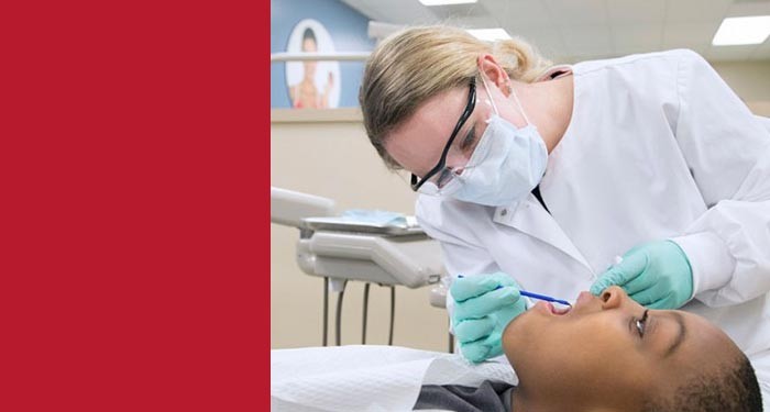 Gateway Dental Assistant student wearing gloves and a white coat exams a patient's teeth in a dental clinic.