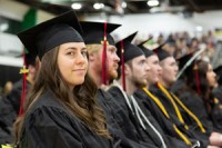 Row of new Gateway graduates sitting at commencement in caps and gowns, the closest smiling.