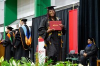 New Gateway graduate in cap and gown shows off her diploma as she walks across the stage.