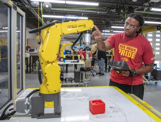 Gateway Electromechanical Maintenance Technician student operates a FANUC robotic arm in an industrial workshop setting.