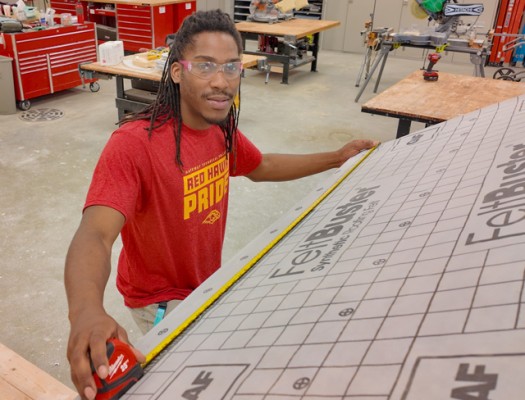 Gateway Building Trades – Carpentry student measures roofing felt for a building project.