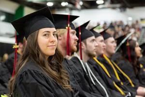 Row of new Gateway graduates sitting at commencement in caps and gowns, the closest smiling.