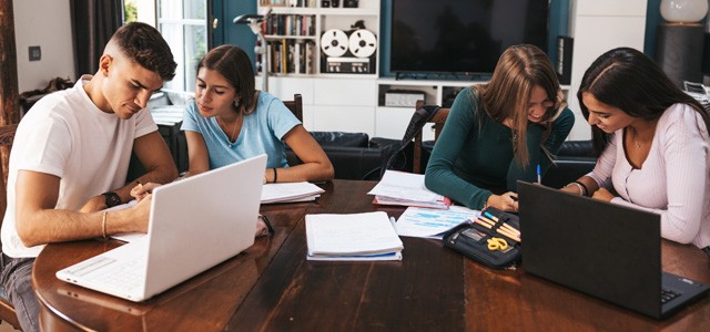 Homeschool students at a table working on schoolwork on laptops