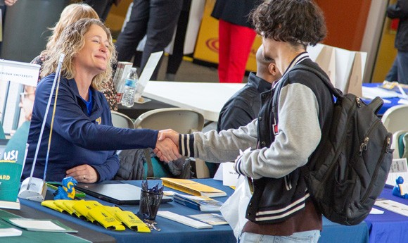 Student at a table at a transfer fair shaking hands with a college representative