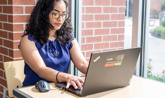 Gateway online student on computer in a common area on campus