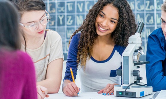 High school student smiling in class with a microscope