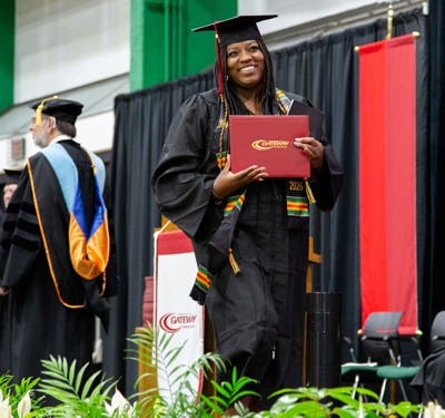 New Gateway graduate in cap and gown shows off her diploma as she walks across the stage.